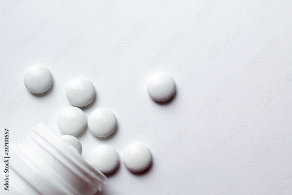 White pills scattered from the medicine bottle on white background. Top view