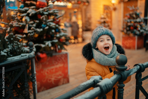 adorable boy with open mouth on the street with decorated christmas trees on the background © Natalia