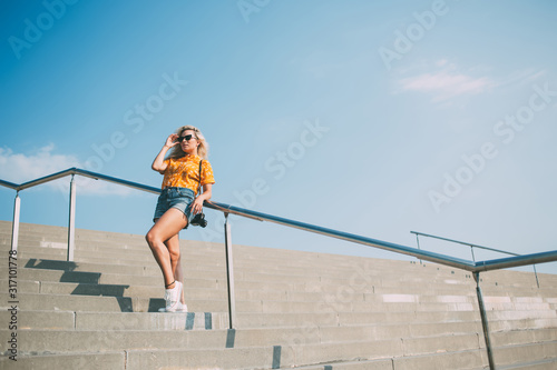 Stylish resting woman in casual wear and sunglasses leaning on railing at city street © BullRun