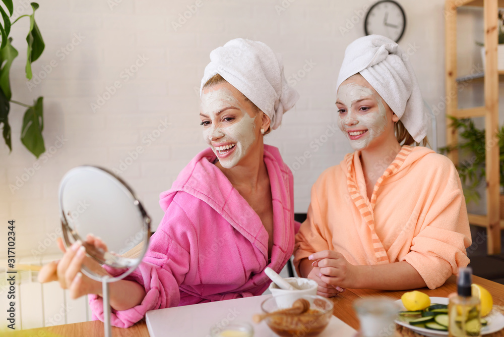 Mother and daughter in bathrobes and towels on head using natural cosmetics and having fun together at home Mother and daughter in bathrobes and towels on head using natural cosmetics and having fun together at home