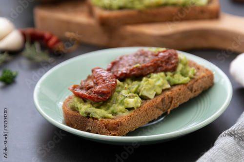 Healthy food. Rye bread with guakomole, avocado pasta and dried tomatoes, on wooden cutting board. Avocado toast.