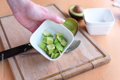 Frauenhand hält Schälchen mit Avocado-stücken, die zuvor geschnitten wurden photo