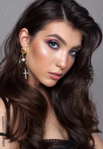 Close up portrait of a very beautiful brunette model with professional purple makeup, perfect skin and gold earrings.