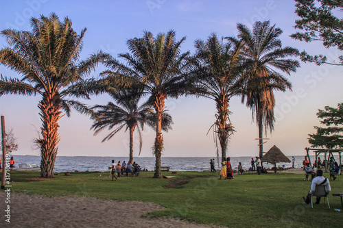 Kampala, Uganda - February 20, 2015: locals relax on the shore of Lake Victoria among palm photo