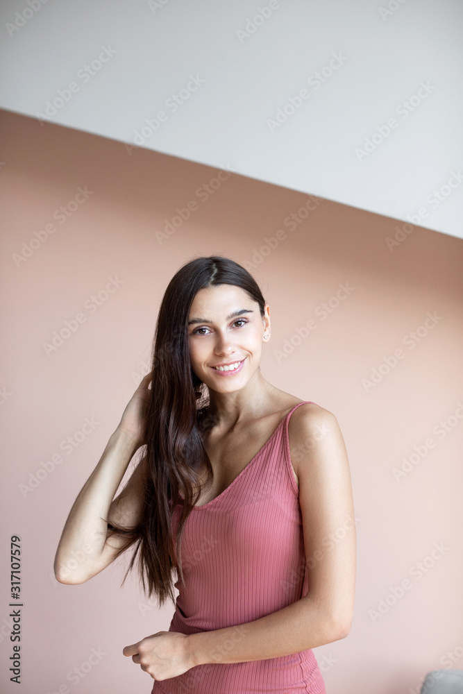 Obraz premium Beautiful woman with long hair is smiling indoors on wall background.