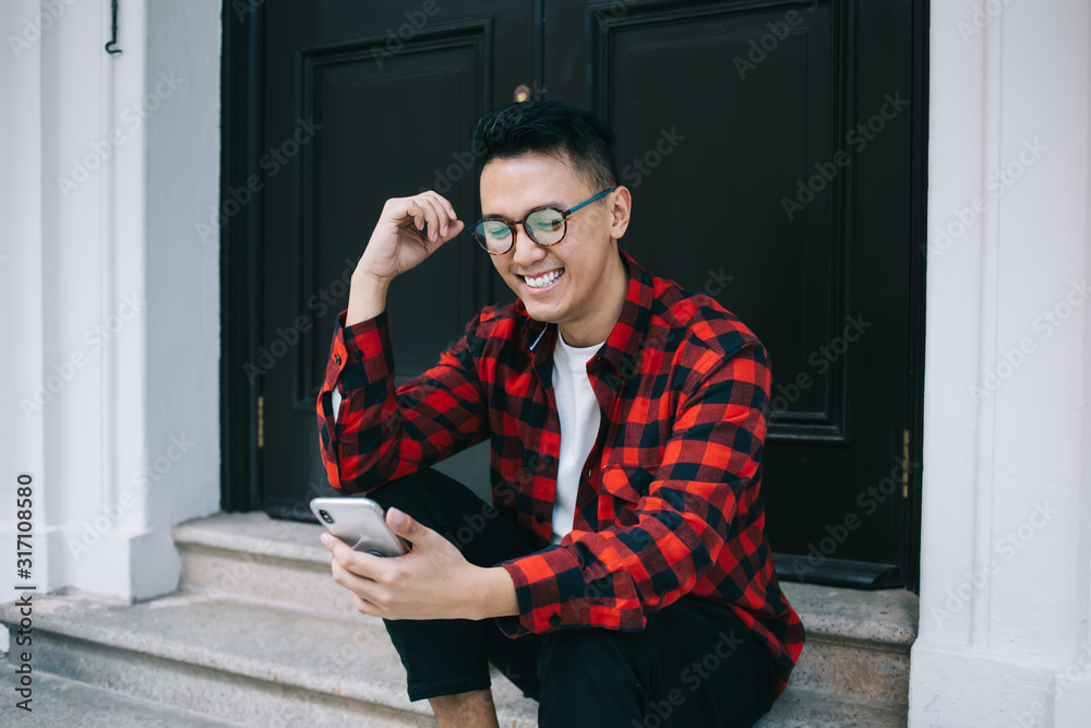 Happy young ethnic man enjoying pastime with smartphone on stairs Happy young ethnic man enjoying pastime with smartphone on stairs