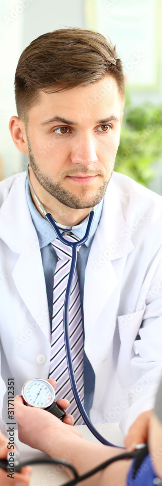 Fototapeta premium Portrait of intelligent doc sitting in comfy clinic chair and talking with troubled patient about state of health. Serious therapist wearing white robe and stethoscope. Medical treatment concept