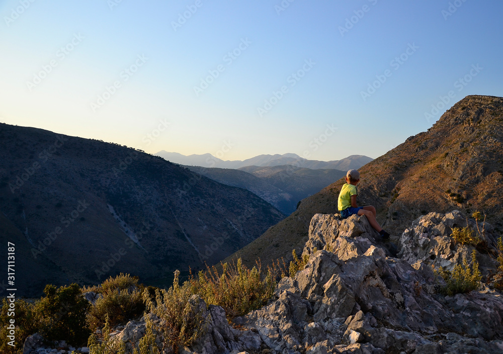 Young boy seating on the stones and looking to mountain perspective.