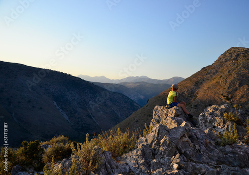 Young boy seating on the stones and looking to mountain perspective.