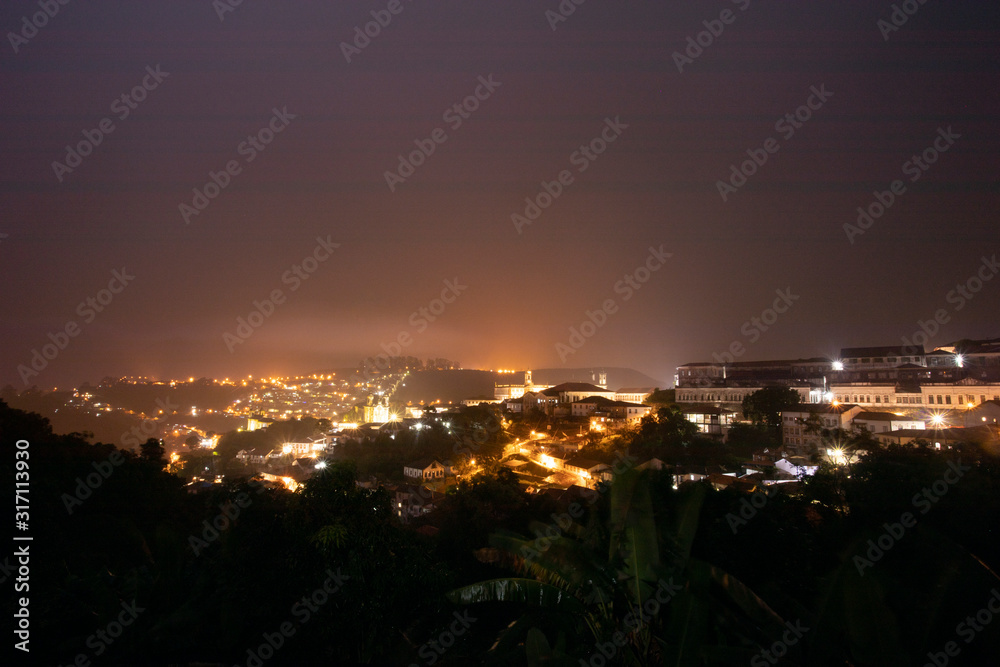 Naklejka premium City lights of the historic city centre of Ouro Preto, Brazil, glowing in the rainstorm and reflecting in the clouds lighting up the night sky
