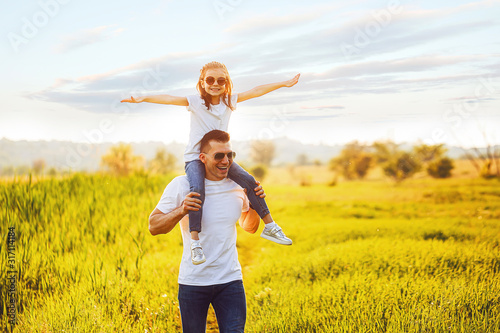 Little girl sitting on father's shoulders and laughing. Summer day, happy family and summer lifestyle concept. Copy space for text.