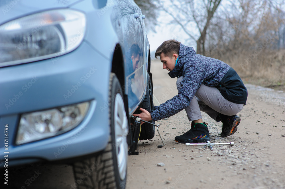 A man broke a wheel on a car and changes it on his own on the road.