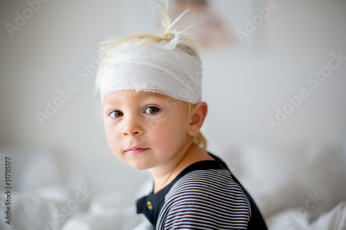 Obraz na płótnie Close portrait of little toddler boy with head injury, sitting in bed, tired