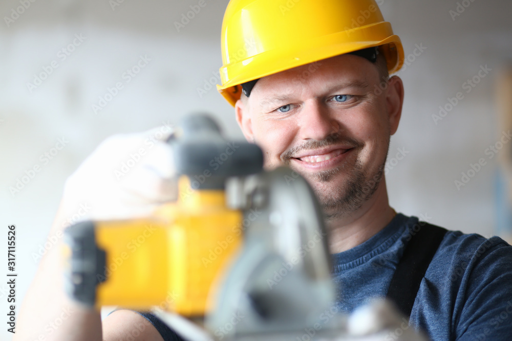Portrait of smiling builder using modern power equipment in order to make work easier. Smart guy holding electric saw carefully and joyfully. Building concept