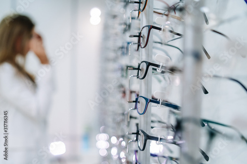 Fototapeta Naklejka Na Ścianę i Meble -  Row of glasses at an opticians. Eyeglasses shop. Stand with glasses in the store of optics. Woman chooses spectacles. Eyesight correction.