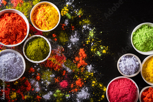 Holi festival celebration. Traditional Indian Holi colours powder decoration with paints. Top view of Organic Gulal colors in bowls, spices, rustic on black background for Holi festival. © Siam