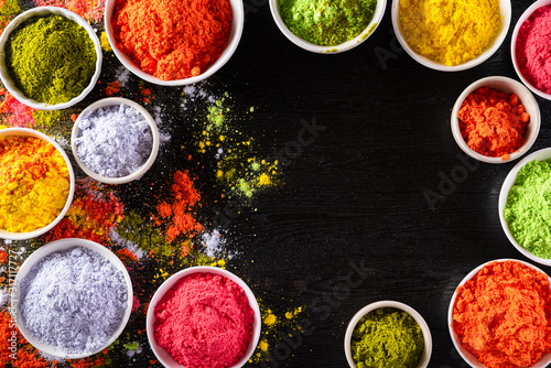 Holi festival celebration. Traditional Indian Holi colours powder decoration with paints. Top view of Organic Gulal colors in bowls, spices, rustic on black background for Holi festival. © Siam
