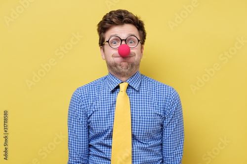 Young handsome man with red clown nose blowing cheeks.