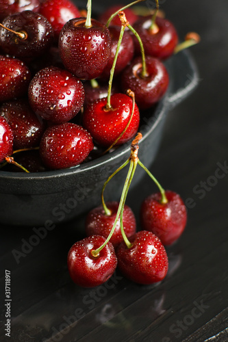 Fresh sweet cherries with water drops in bowl on dark rock table.