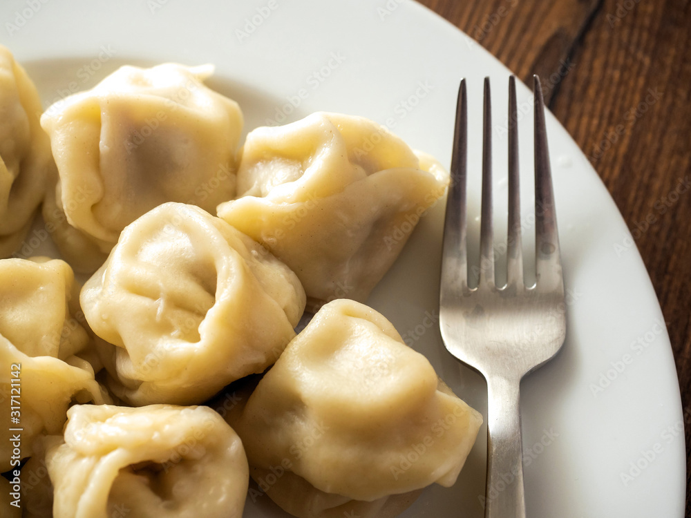 Portion of traditional Russian cooked dumplings on a white plate with metal fork on wooden table,