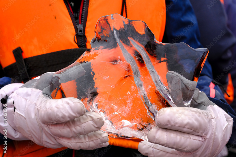 Fototapeta premium Young woman is taking a boat trip to Jokulsarlon Glacier Lagoon in Iceland. She is holding a large piece of ice