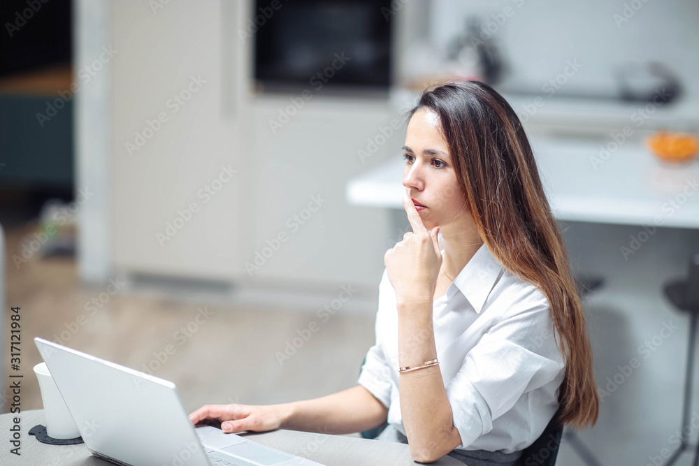 young Caucasian woman in a modern office is working behind a white laptop in business clothes. young Caucasian woman in a modern office is working behind a white laptop in business clothes.