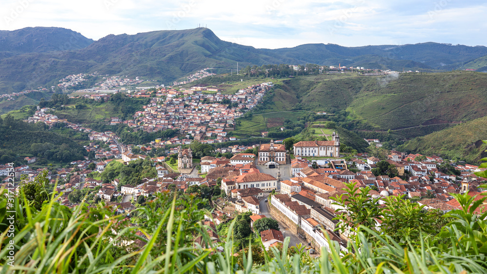 Panorama landscape with historic colonial city of Ouro Preto seen from the São Sebastião viewpoint with Itacolomi mountain in the background on an overcast morning with grass in the foreground