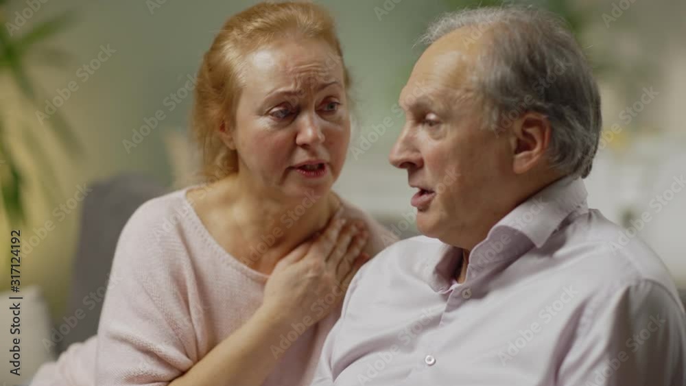 Elderly wife trying to comfort stressed angry husband looking at paper bills and being nervous about large expenses Elderly wife trying to comfort stressed angry husband looking at paper bills and being nervous about large expenses