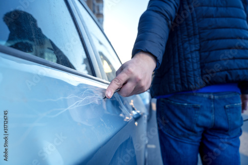 Bad guy scratching the car door with a screwdriver in the parking lot on the street. Damage of property from revenge for treason or betrayal, or threat. Auto insurance fraud or vandalism.