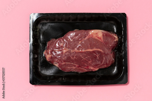 Black plastic pack with fresh beef steak isolated on pink background. Raw meat packed without label top view, vacuum packed