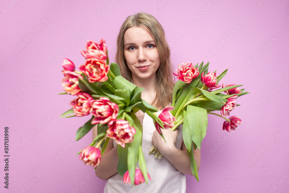 young girl holds a bouquet of flowers on a pink background, a happy woman with tulips gives flowers, offers to buy