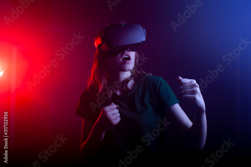 girl gamer in virtual reality glasses plays boxing on a dark red-blue background, a woman begins a virtual hand-to-hand fight