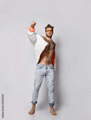 Young confident sexy man in damaged jeans, jacket and wreath on head standing barefoot
