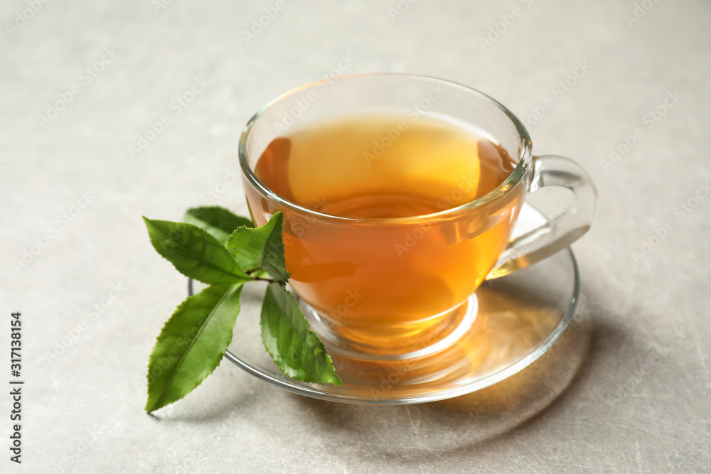 Cup of green tea and leaves on grey table Cup of green tea and leaves on grey table