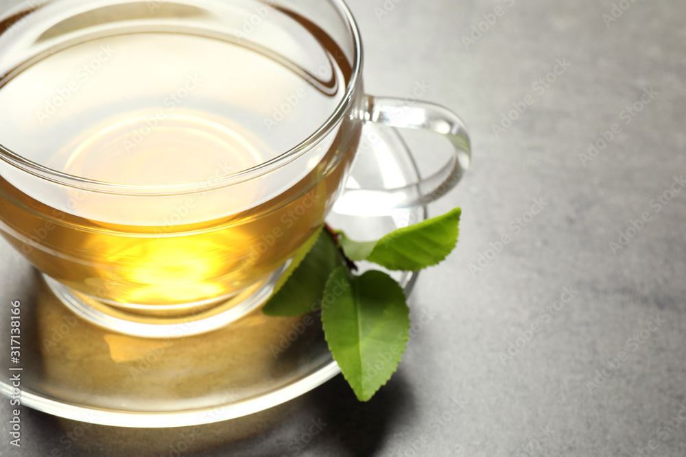 Cup of green tea and leaves on grey table, closeup. Space for text Cup of green tea and leaves on grey table, closeup. Space for text