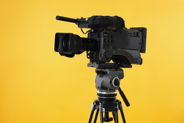Modern professional video camera on yellow background