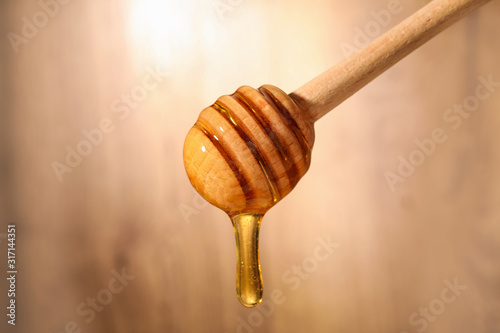 Dripping honey from wooden dipper on blurred background, closeup