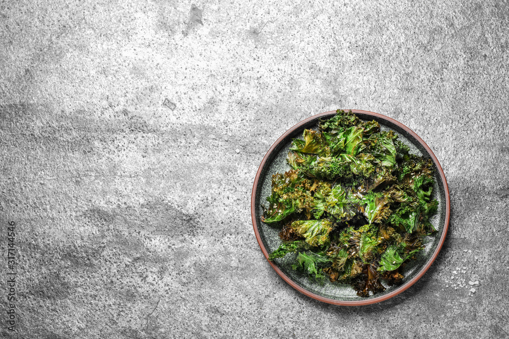 Tasty baked kale chips on grey table, top view. Space for text