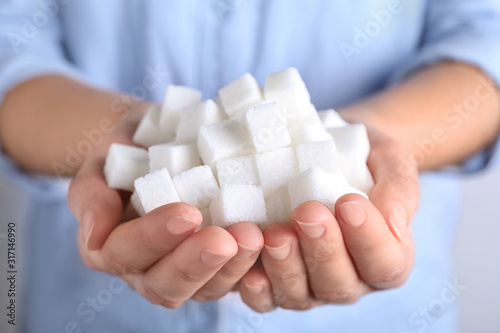 Woman holding heap of refined sugar cubes, closeup