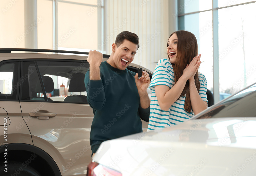Happy couple with car key in modern auto dealership Happy couple with car key in modern auto dealership