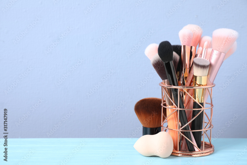 Set of professional makeup brushes in holder on blue wooden table. Space for text - obrazy, fototapety, plakaty 