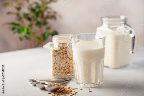 Vegan oat milk, non dairy alternative milk in a glass. Oat flakes  on stone table.