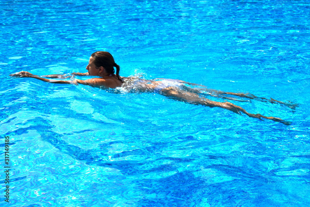 A woman swims in the pool. Slender young girl floats