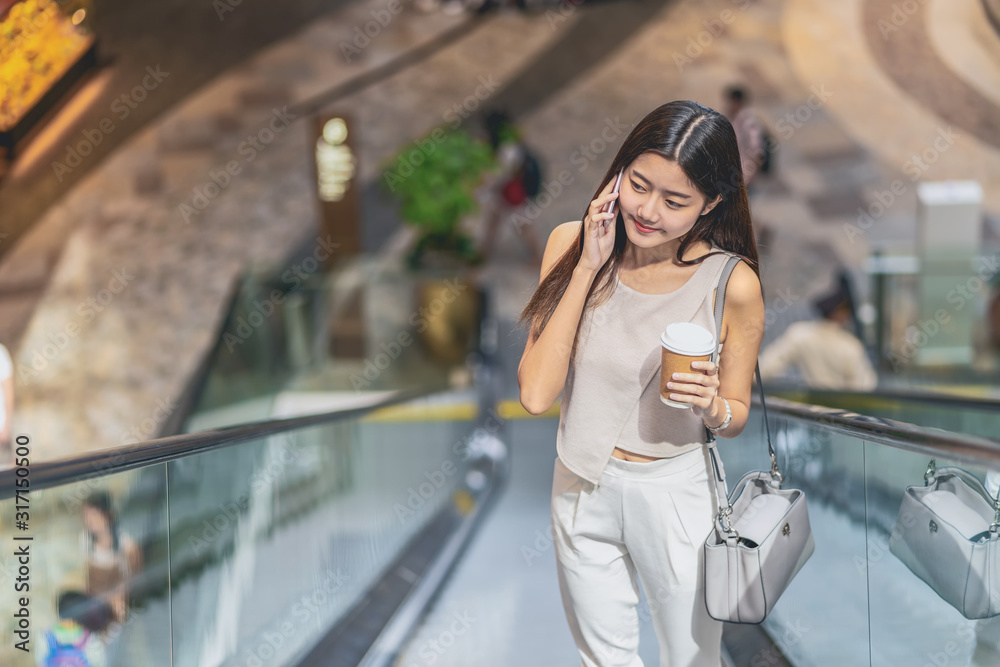 Young Asian woman passenger using smart mobile phone and walking up escalator in department store when traveling in city,japanese,chinese,Korean lifestyle and daily life,commuter and transportation