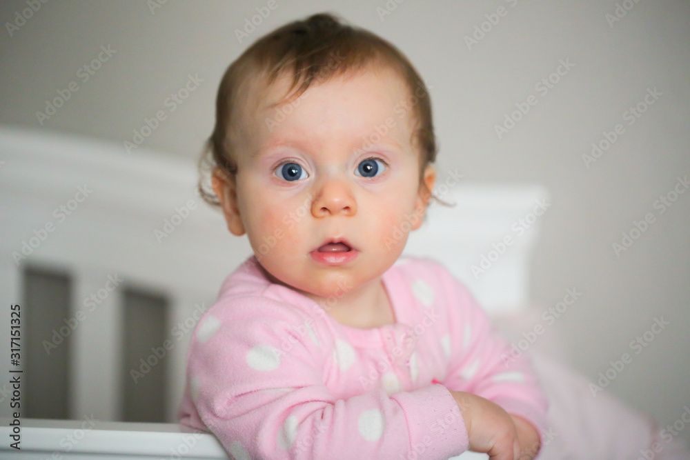 Very Cute 10 Month Old Baby Girl with Big Blue Eyes Playing in the White Crib