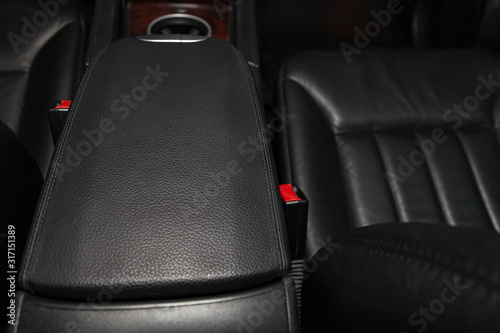 Fényképezés Close-up on the car front armrest with black leather trim, buttons and seat belt in the interior after detailing and dry cleaning