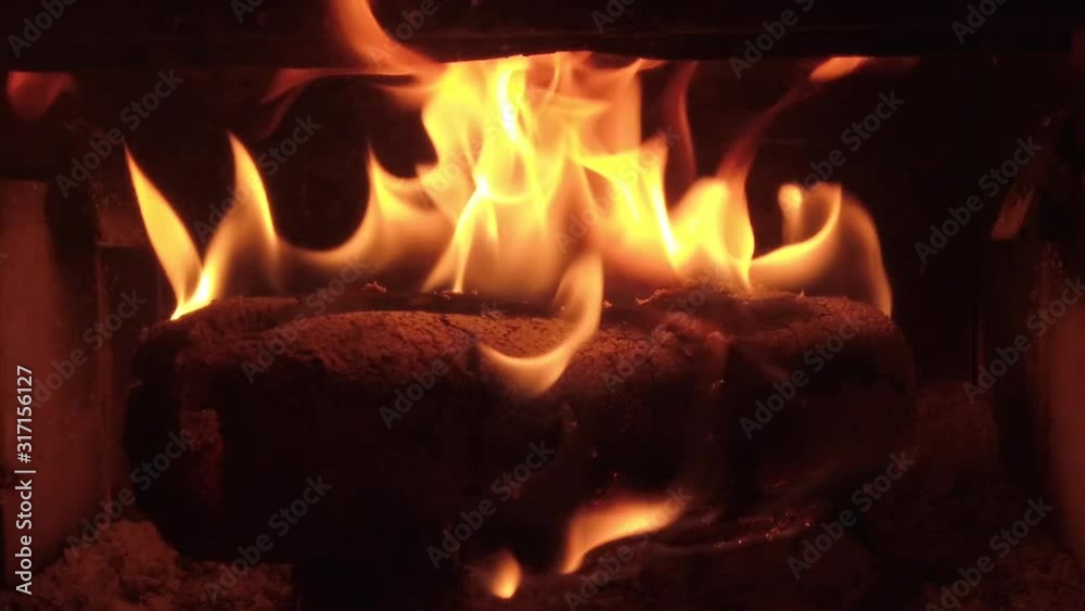 Yellow flames licking burning on a single log in a cast iron wood burning stove, orange and red coals, deep black contrast, slow motion Yellow flames licking burning on a single log in a cast iron wood burning stove, orange and red coals, deep black contrast, slow motion