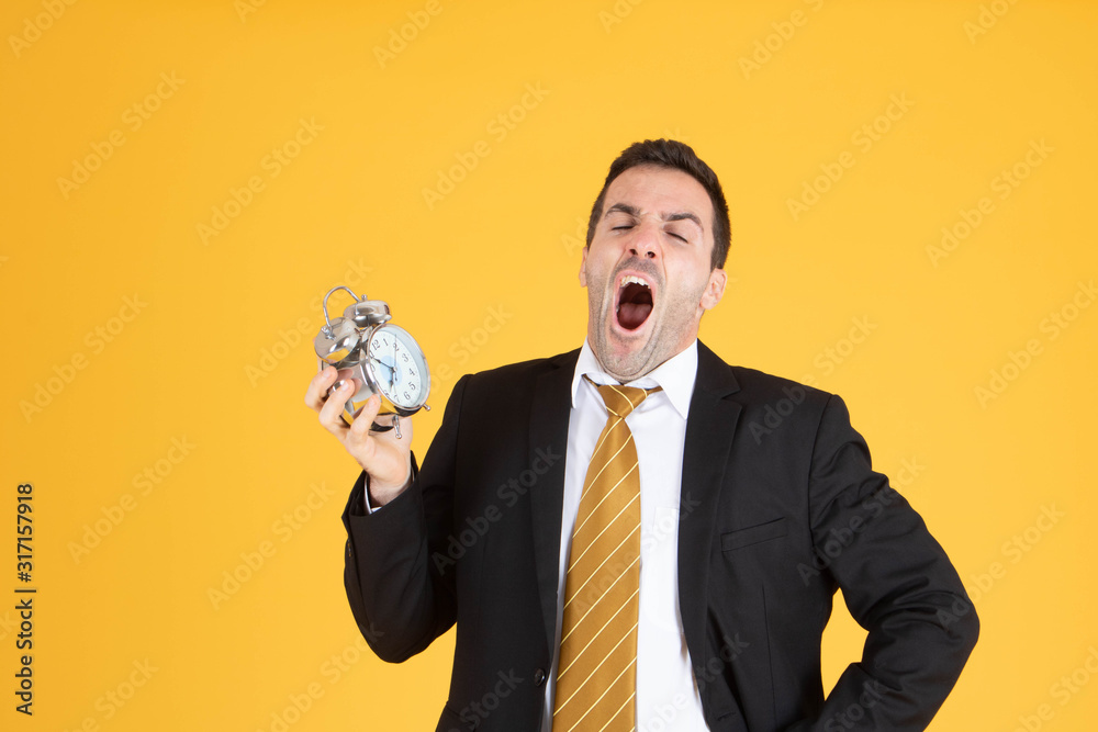 Portrait of a handsome businessman holding clock feeling sleepy and tired on yellow background. Portrait of a handsome businessman holding clock feeling sleepy and tired on yellow background.