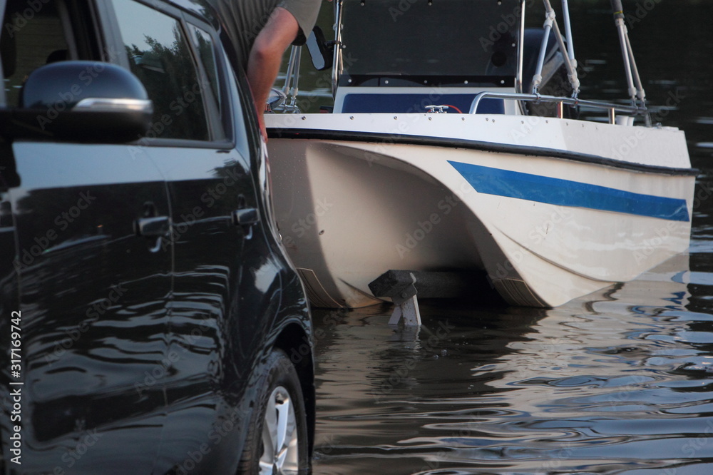 White motor boat launch, a man puts a boat on the car trailer in water on shipway