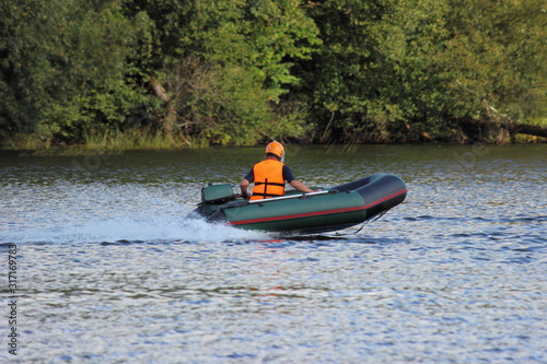 Dark green little Inflatable outboard motor boat with pilot racer in orange lifejacket and helmet fast drive on water Race at river on a Sunny summer day, outdoor sport competition